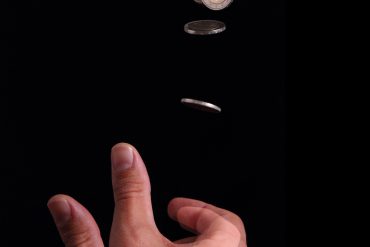 Layered multi-shot image of a hand flipping a coin and the coin in different stages of the coin toss.