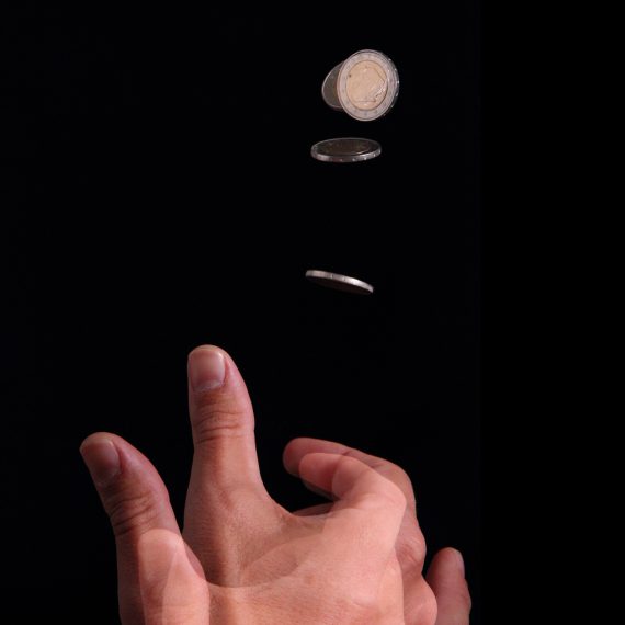 Layered multi-shot image of a hand flipping a coin and the coin in different stages of the coin toss.