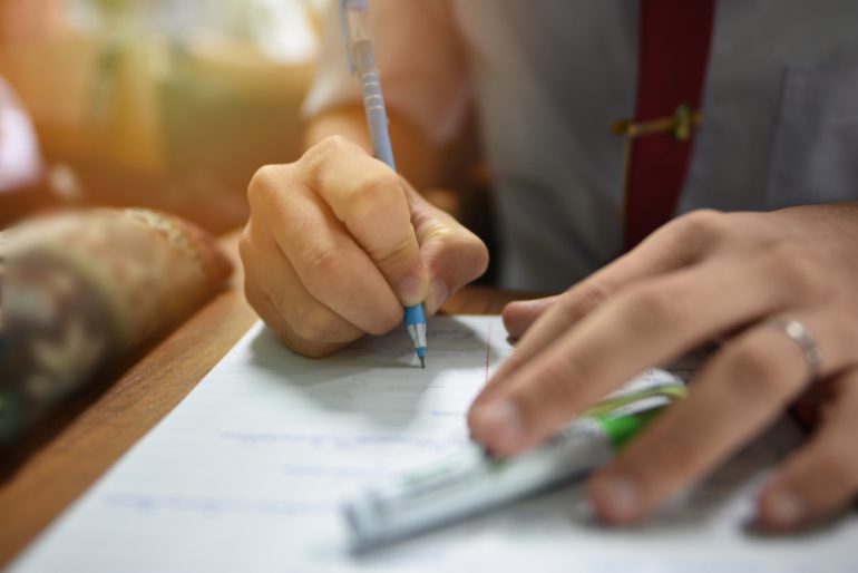 Student holding a pen taking lecture note or doing writing assignment in the classroom; closed up photo of young learner using a pen during the written test in collage or university training center - Image