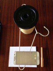 Smartphone suspended above a writing pad by a coathanger weighted down by an elevated weight