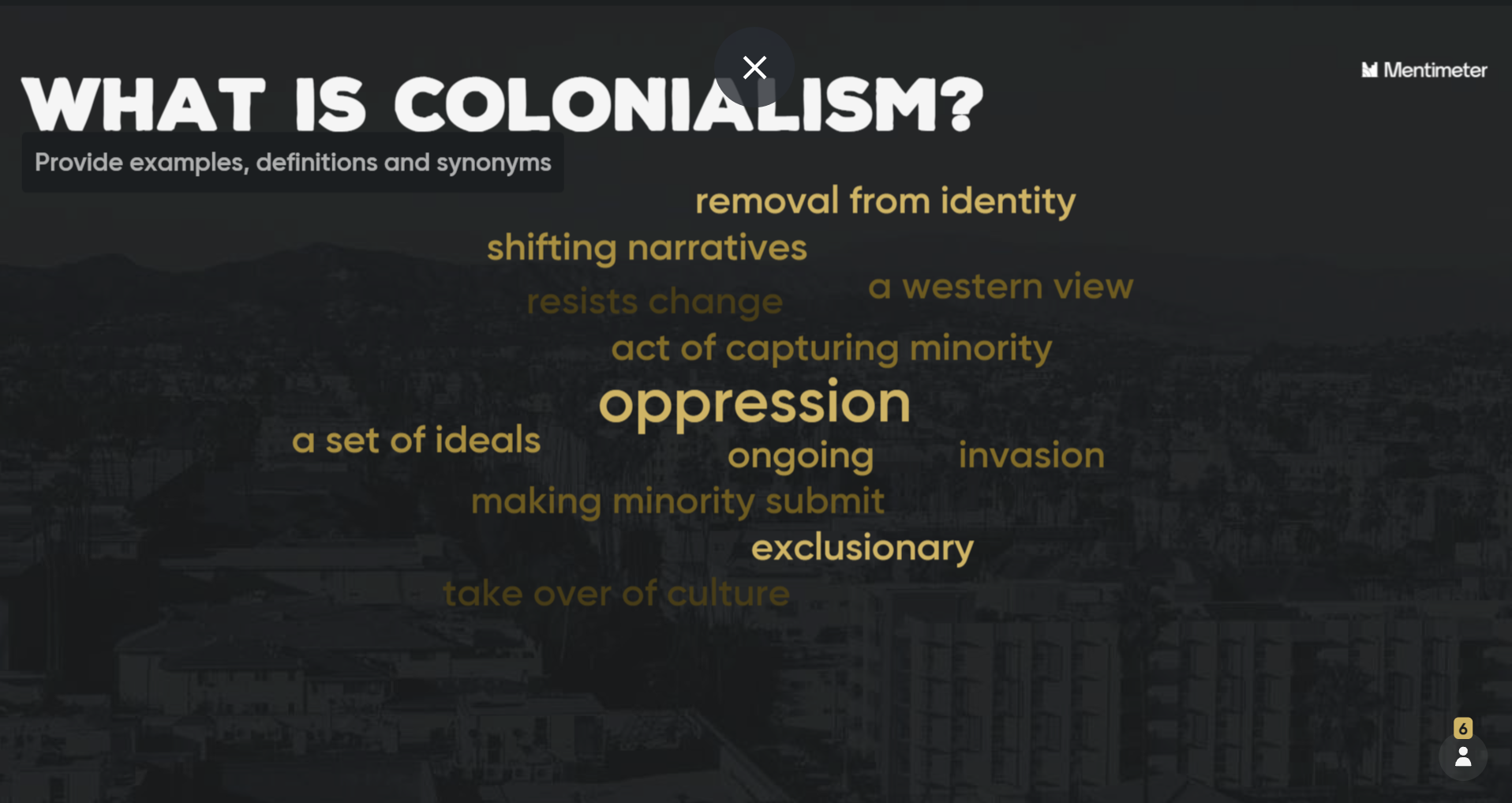 A screenshot of a word cloud slide with light coloured text against a contrasting dark monochromatic background of a picture of a town. The question, “What is colonialism” is in bold, white, all-caps text on the top left-hand side of the slide with sub-text underneath in smaller, writing underneath stating “Provide examples, definitions and synonyms”. The word cloud text is in various shades of gold with the following words and phrases (listed from biggest and boldest to lightest): oppression, removal from identity, exclusionary, shifting narratives, ongoing, a set of ideals, act of capturing minority, making minority submit, invasion, a western view, resists change, and take over of culture.