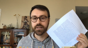 Matthew, wearing dark-rimmed glasses and with a beard, holds a printedcopy of a weekly reading. 