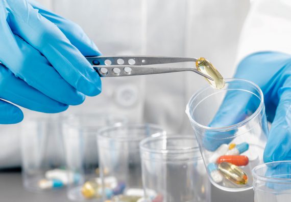 A close up image of pills of different sorts being sorted into jars by a person in a white coat with blue disposable gloves.