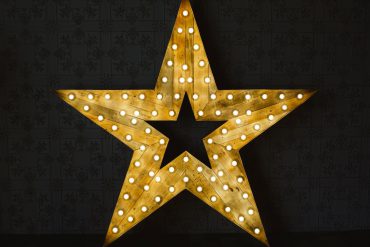 Wooden star with light bulbs. shining on a stage on top of a black background.