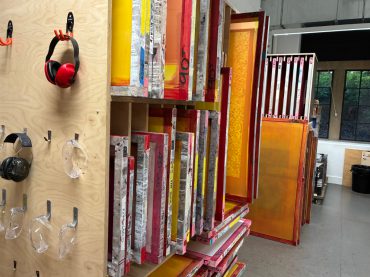 Screen print studio, with colourful washed up screens in a rack and tools hanging on a plywood board