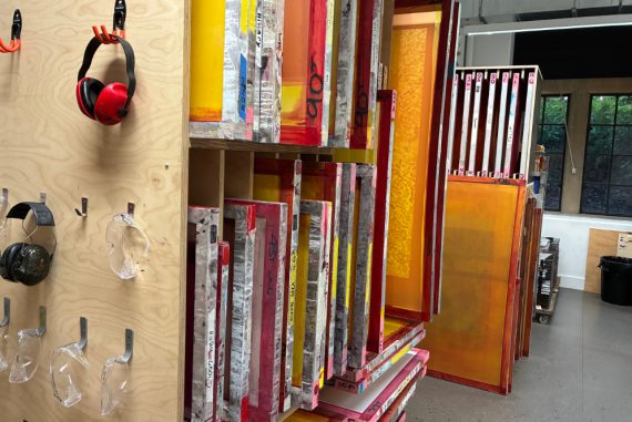 Screen print studio, with colourful washed up screens in a rack and tools hanging on a plywood board