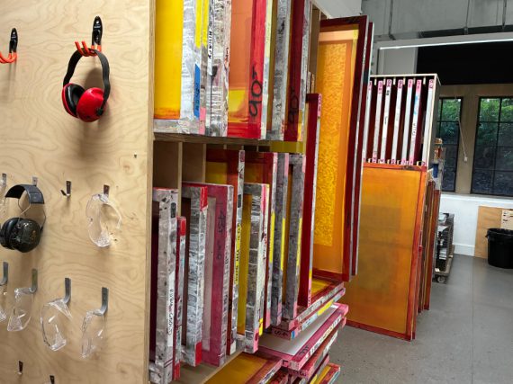 Screen print studio, with colourful washed up screens in a rack and tools hanging on a plywood board