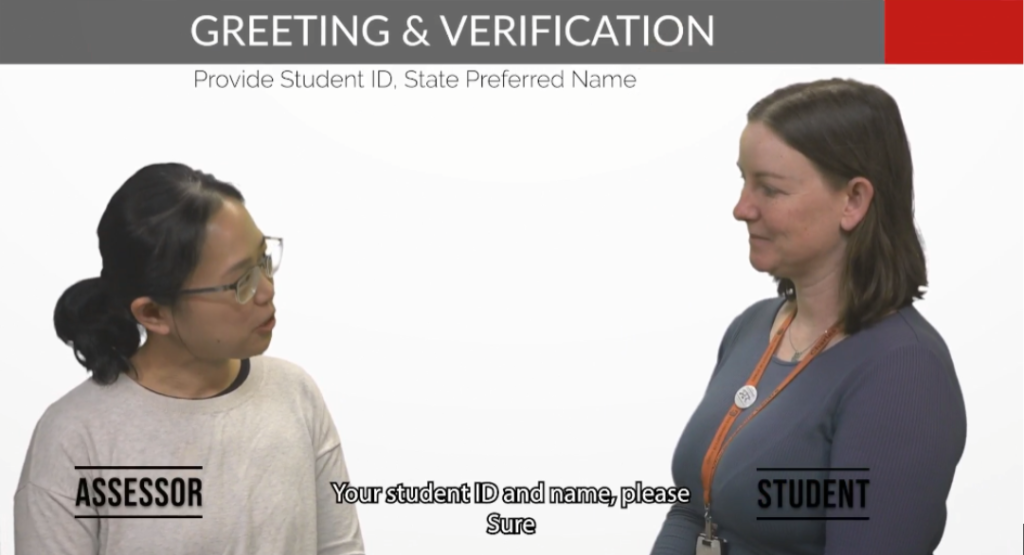 Screenshot from a mock IOA video showing an assessor and student in conversation. The header reads 'Greeting & Verification: Provide Student ID, State Preferred Name' with subtitle text showing the assessor requesting the student's ID and name.