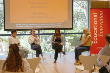 Student panel and MC sit speaking at the End of Year event in front of a slide screen with a big window and garden beyond.
