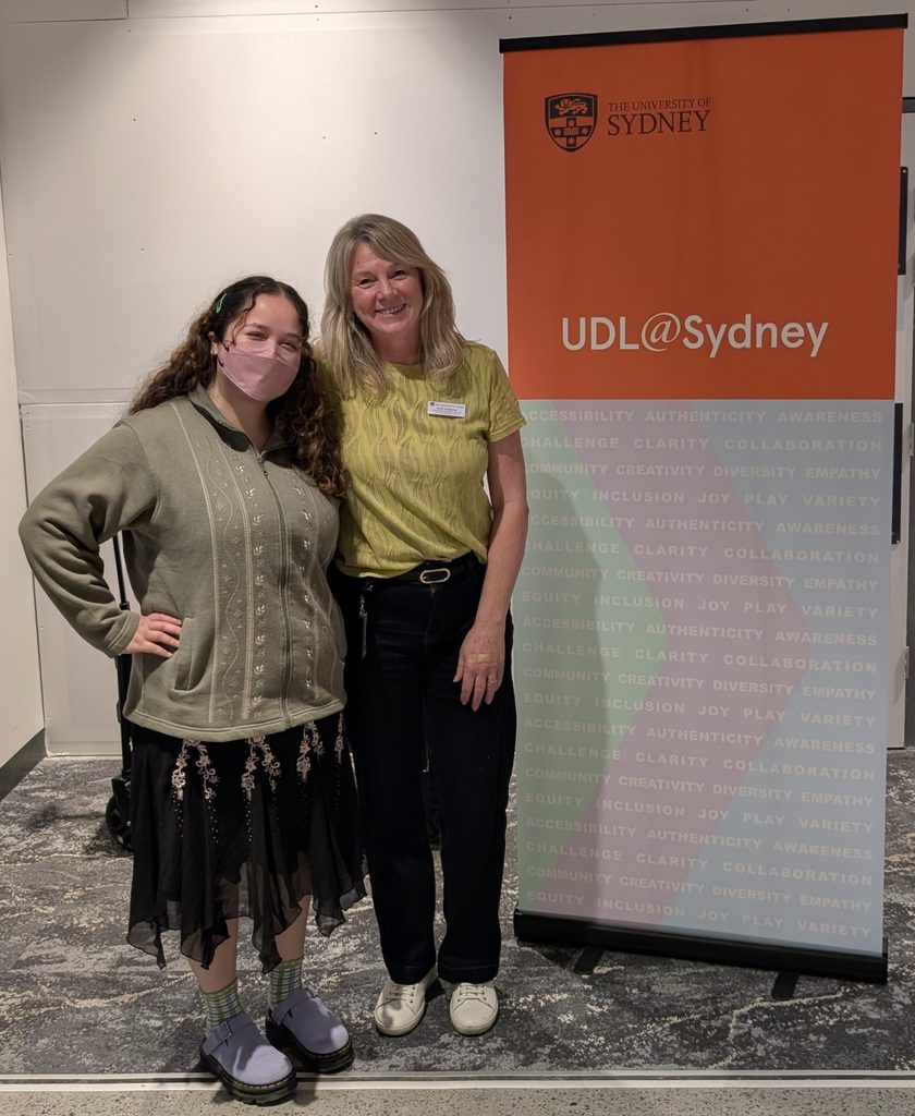 Sarah and Kayla are standing in front of a 'UDL@Sydney' banner looking happy.